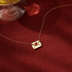 Détail d'un collier enveloppe en or 18K avec zircon coeur rouge sur tissu rouge texturé