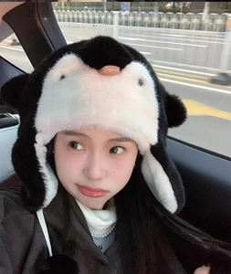 Close-up of soft penguin plush hat with earflaps worn by a girl in a car interior