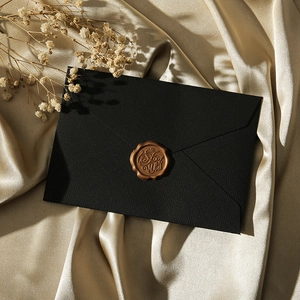 Detailed view of a black envelope with a gold 'For You' wax seal on satin fabric