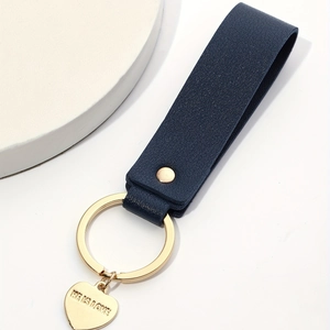 Detail of dark blue leather loop keychain with golden heart charm and HE IS LOVE engraving