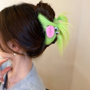 Detail of a plush green monster hair claw clip with pink lips on a woman's hair