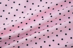 Detailed macro view of smooth pink polyester fabric with black polka dots pattern