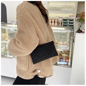 Detail showing a black velvet envelope crossbody bag with a gold chain on a model