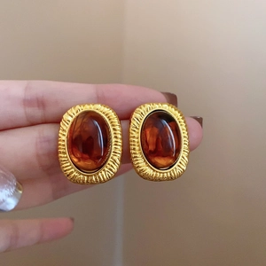 Macro detail of hand holding gold-plated irregular earrings with amber stones