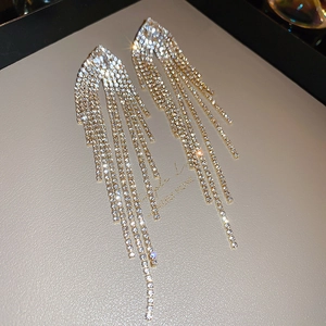 Macro detail of luxury sparkling long tassel earrings with pavé rhinestones in gold finish