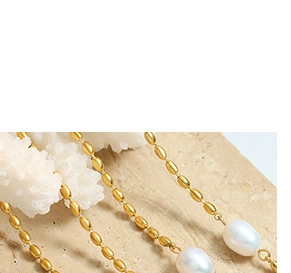 Detail of golden beaded chain with a white irregular pearl pendant on stone surface