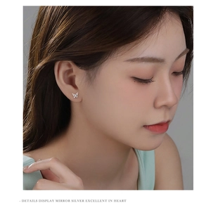 Detailed close-up of a delicate silver butterfly stud earring worn on the earlobe