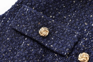 Macro shot of navy blue sequined tweed fabric with an embossed gold metal button
