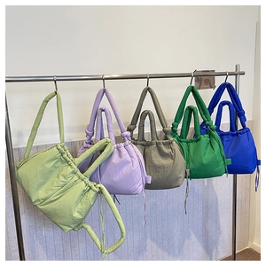 Row of colorful nylon drawstring tote bags in green, purple, and blue on a metal rack