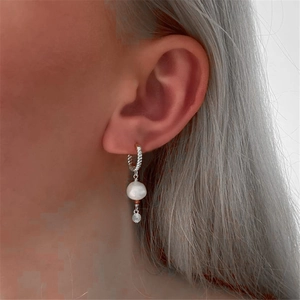 Macro detail of S925 silver twist hoop earring with star-accented white pearl