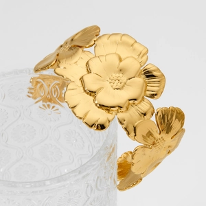Elegant gold flower open bangle bracelet hanging on a crystal glass rim for a premium look