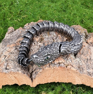Gothic style stainless steel snake bracelet with green eyes on a natural bark background