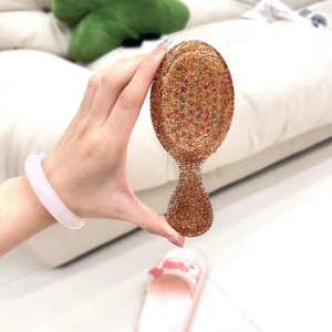 Close-up of portable mini hairbrush with gold glitter and sequins in transparent plastic