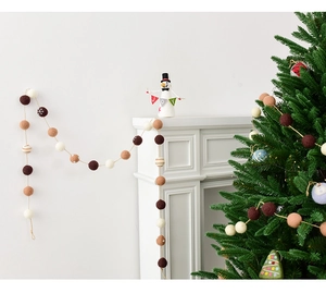 Detail of wool felt ball garland in earthy tones with snowflake embroidery on a fireplace