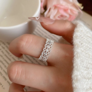 Close-up of elegant silver lace hollow flower ring on finger with white roses and books