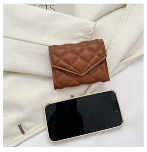 Brown quilted leather wallet on beige fabric next to a smartphone for size reference
