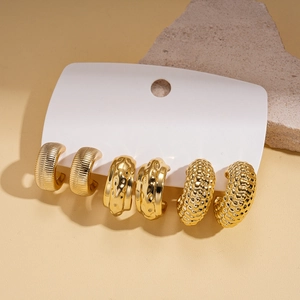 Dettaglio di tre paia di orecchini dorati con diverse texture su espositore bianco