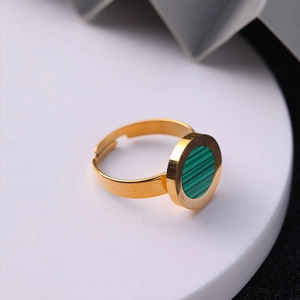 Close-up of golden adjustable ring with circular green malachite pattern on a white stand