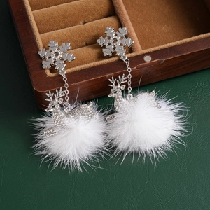 Detail of silver reindeer earrings with white pompom and crystal snowflakes on wood