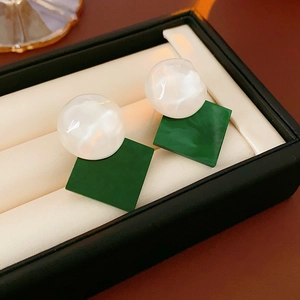 Detail view of white sphere and green resin earrings in a black premium jewelry box