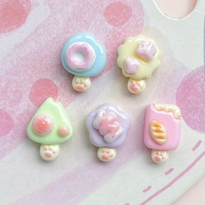 Flat lay of miniature resin donuts and ice cream charms with paw prints on pink backdrop