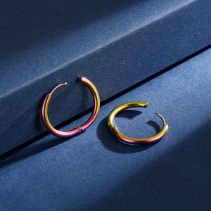 Close-up of rainbow gradient stainless steel hoop earrings on a textured blue display