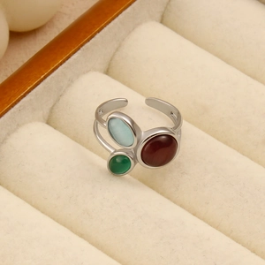 Détail d'une bague ouverte argentée avec trois gemmes ovales colorées sur velours