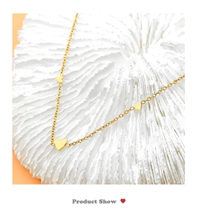 Detailed view of gold titanium steel chain with three heart pendants on a textured stone