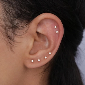 Macro shot of six mini gold-plated stud earrings set with sparkling cubic zirconia on ear