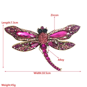 Detailed macro view showing a crystal dragonfly brooch with dimensions and material labels