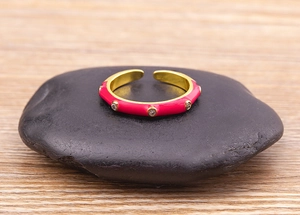Macro shot of pink enamel gold plated ring with inlaid zircons on a smooth black stone