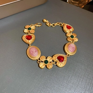 Detail of vintage gold necklace with red heart stone, green clover, and pink cameo charm