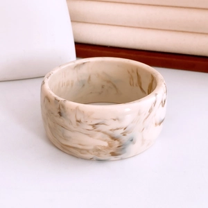 Close-up of minimalist cream resin bangle featuring brown marble patterns and glossy finish