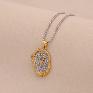 Macro detail of a gold V-letter pendant set with clear crystals on a silver ball chain