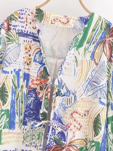 Detailed view of vibrant tropical plant and animal prints on white V-neck blouse