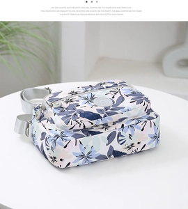 Macro detail of floral nylon crossbody bag featuring multiple zipper pockets and wide strap