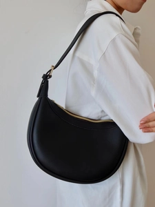 Close-up of minimalist black leather crescent hobo bag with gold zipper and hardware
