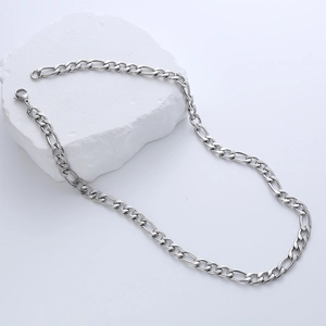 Detailed view of silver stainless steel Figaro chain necklace coiled on white stone