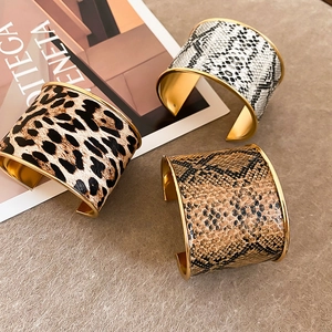 Detail view of wide leopard and snake print C-shaped gold-plated metal cuffs