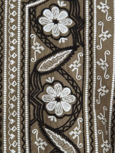 Detail of ethnic embroidery with floral and geometric patterns on brown linen fabric