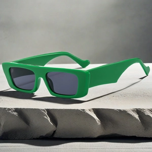 Detail view of green rectangular sunglasses with wide frames on a textured stone surface