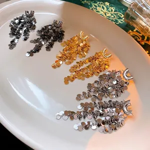 U-shaped sequin tassel earrings in gold, silver, and black on a ceramic tray