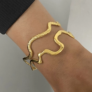 Detail of wave-shaped gold stainless steel bangles with smooth and hammered textures