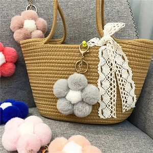 Macro detail of fluffy plush flower keychains in multiple colors hanging on a woven bag