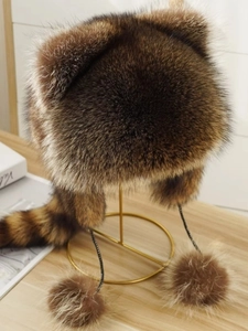 Detail of faux fur raccoon hat with striped tail and ear flaps on metal stand