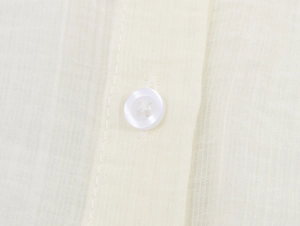 Close-up of white four-hole button and textured translucent gauze fabric on the blouse