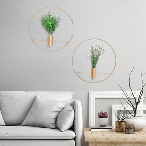 Set mit zwei goldenen Metall-Wandvasen mit künstlichem Grün an einer grauen Wand