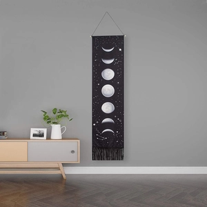Lunar eclipse cycle tapestry with moon phases and fringe hanging on a gray wall