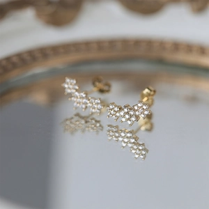 Macro detail of gold flower earrings with pavé set crystals on a reflective tray