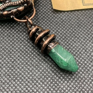 Detailed macro view of green hexagonal crystal pendant wrapped in bronze wire jewelry